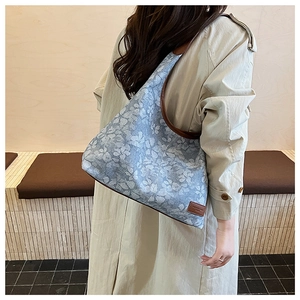 Detail of blue denim tote bag with daisy print and brown leather trim worn by a model