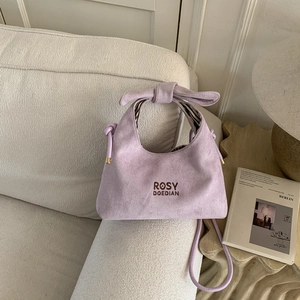 Detail view of lavender suede handbag with bow knot handle and striped fabric lining