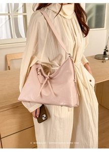 Minimalist light pink tote bag with glossy leather and decorative strap shown on a desk