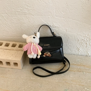 Close-up of black leather handbag with golden clasp and cute white plush bunny charm