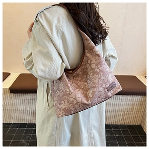 Detail of floral shoulder bag with leather handles and decorative brand label on fabric