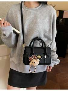 Elegant black lychee leather handbag with golden buckle and plush bear pendant detail
