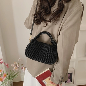 Close-up of black woven bucket bag with elegant round handle and golden metal buckle details