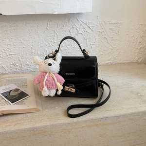 Detail of black leather square handbag with gold twist lock and white plush pendant