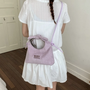 Detail of light purple suede crossbody bag with knot decor and striped lining worn by model