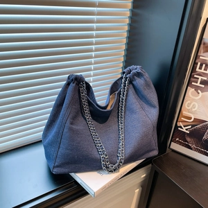 Détail d'un cabas en denim bleu avec plis à cordon et bandoulière en chaîne tressée