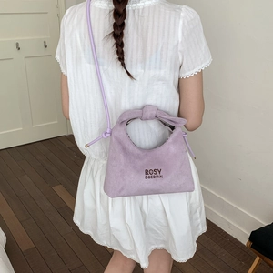 Close-up of lavender suede handbag with knot handle detail and thin shoulder strap