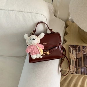 Detail of burgundy glossy leather handbag with a plush bear charm on white sofa