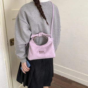 Detail of light purple suede handbag featuring bow handle and brand logo print