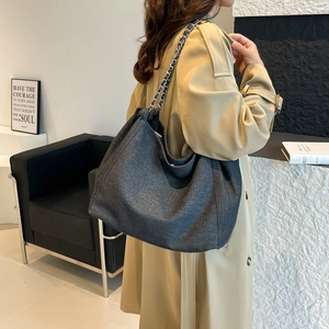 Détail d'un cabas en denim gris avec chaîne en métal argenté et bandoulière en cuir