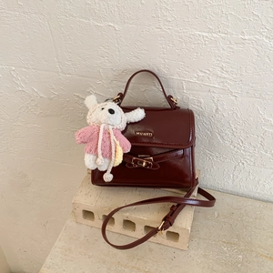 Detailed close-up of a burgundy leather crossbody bag with metal twist lock and rabbit charm