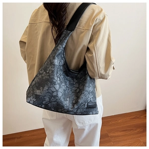 Detail of grey floral canvas tote bag with black leather trim worn over the shoulder
