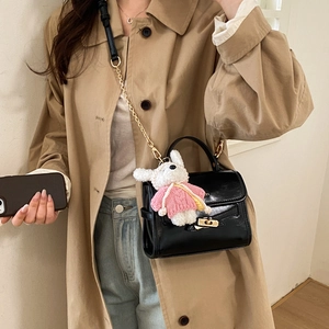 Detail of black patent leather crossbody bag with gold twist lock and cute bunny pendant