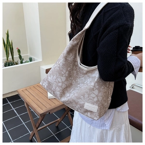 Detail of floral canvas tote bag with a white brand logo tag and sturdy shoulder strap