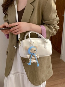 Sac bandoulière en cuir blanc avec poignée et breloque ours porté par un mannequin