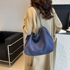 Détail du sac cabas en denim bleu foncé avec bandoulière chaîne sur un trench beige
