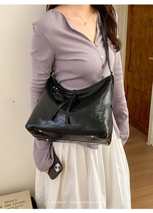 Detail of black glossy bow tote bag featuring wrinkled texture and metal bottom studs