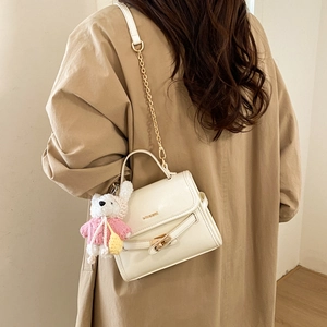Detailed back view of white square handbag with gold chain strap and teddy bear charm