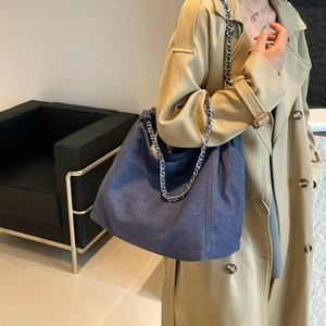Détail du sac cabas en denim bleu avec bandoulière chaîne argentée et forme demi-lune