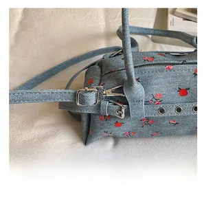 Detail of silver lobster clasp and red floral embroidery on blue denim shoulder bag