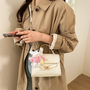 Close-up of a cream-colored leather crossbody bag with a cute teddy bear plush charm