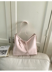 Detail of light pink pleated shoulder bag with glossy texture and fashion tag on sofa