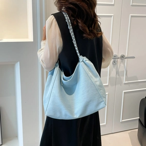 Détail du sac hobo bleu clair avec bandoulière en chaîne et texture de toile sur l'épaule
