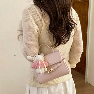 Detail view of pink crossbody bag with gold hardware and plush bunny charm on a model