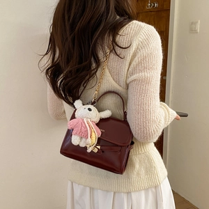 Detail of dark red glossy leather handbag with gold chain and plush bunny charm