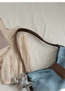 Detail of light blue denim shoulder bag with brown leather strap and silver charms