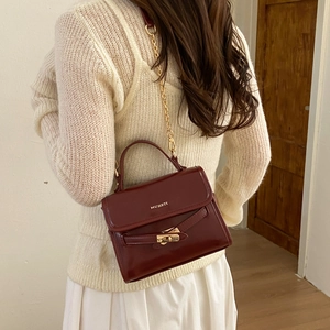 Detail of burgundy leather crossbody bag featuring gold twist lock and metallic chain