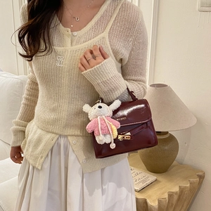 Detail of burgundy leather shoulder bag featuring gold clasp and cute bear pendant charm