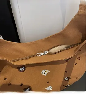 Close-up of cat embroidery and smooth metal zipper detail on brown canvas tote bag