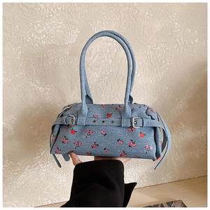 Detail of blue denim handbag with red floral pattern and decorative metal buckles