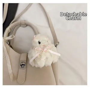 Close-up of beige leather bag featuring a cute white plush animal charm with pearl bow