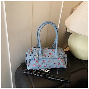 Close-up of light blue denim handbag with red floral print and leather strap buckle