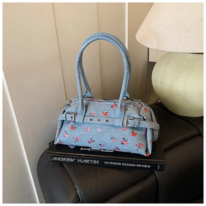 Detailed view of light blue denim handbag with red floral print on a black book decor