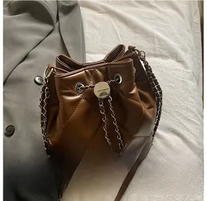 Detail showing brown quilted bucket bag with silver chain strap on white fabric