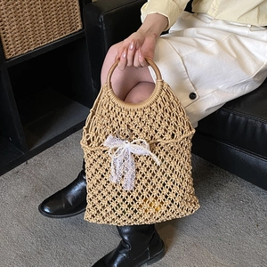 Beige macramé tote bag with wooden handles and pearl bow on a chic beach resort backdrop