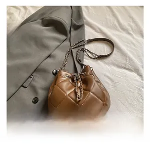 Detail of brown quilted bucket bag with chain strap and drawstring on a grey suit background
