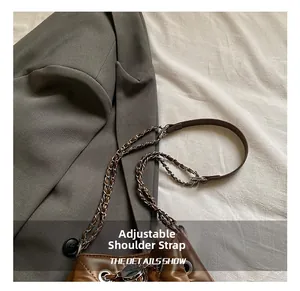 Detail showing the adjustable brown leather and metal chain shoulder strap of the bucket bag