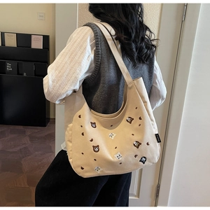 Detail shot of beige canvas tote featuring embroidered bear and cat patterns with side label