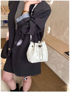 Close-up of white quilted bucket bag with silver chain strap on a model shoulder