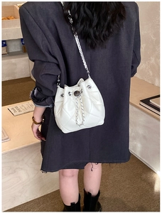 Close-up of a white quilted bucket bag featuring a silver chain strap and drawstring detail