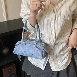 Detail of blue floral handbag with silver buckles and red flower patterns on denim fabric