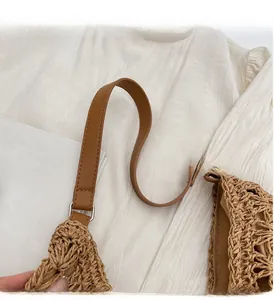 Detail of woven straw tote bag with brown leather shoulder strap and metal buckle