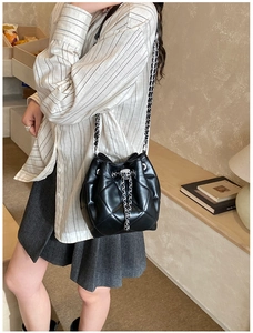 Chic black quilted bucket bag with chain strap shown on model in a minimalist room