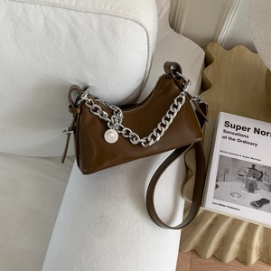 Close-up of brown faux leather half-moon bag featuring a thick silver chain and metal charm
