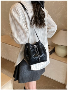Detail of black quilted bucket bag with silver chain strap worn by a model in interior