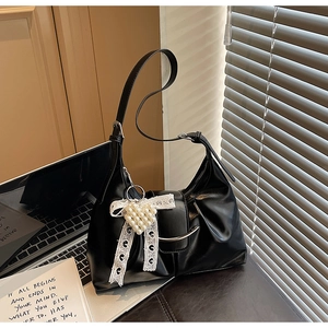 Detail of black tote bag with lace bow, pearl heart charm and metallic bar closure